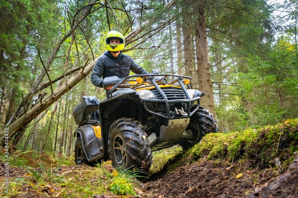 A man in a yellow helmet rides a Quad bike through the woods. Quad bike on a forest road. Journey through the forest on a Quad bike. Sale and rental of ATVs. Driving on bad roads.